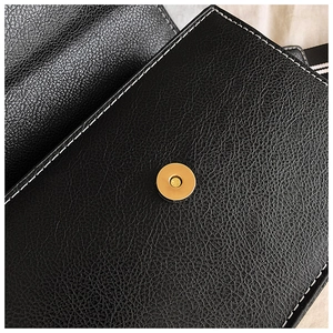 Detail of black lychee grain leather handbag with gold magnetic closure and contrast stitching