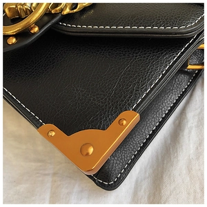 Detail of black lychee leather bag with white stitching and gold metal corner protectors