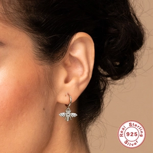 Detailed view of an S925 sterling silver bee charm earring worn on a model's ear