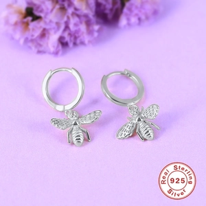Macro shot of 925 sterling silver bee charm earring on purple floral background