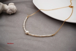 Detail of minimalist gold chain necklace with small white pearls and curved centerpiece