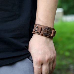 Brown wide leather bracelet with bronze Tree of Life emblem worn on a wrist outdoors