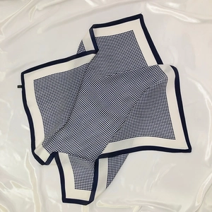 Elegant houndstooth silk-like square scarf laid on white fabric with natural lighting