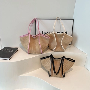 Three oversized woven straw tote bags in pink, white, and black trim colors on white stairs