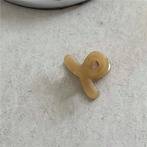 Detailed close-up of a cream-colored acetate mini hair claw clip on a textured surface