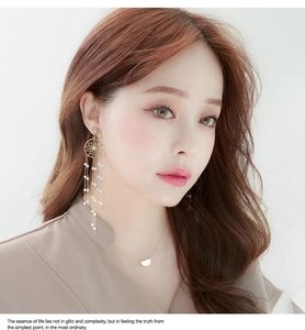 Detail of elegant gold-tone long tassel earrings with pearls on a female model