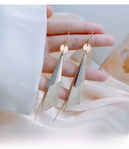 Macro detail of geometric long gold earrings with layered metallic triangle pendants