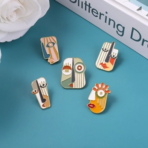 Detailed view of five abstract face enamel pins with colorful geometric art on a blue background