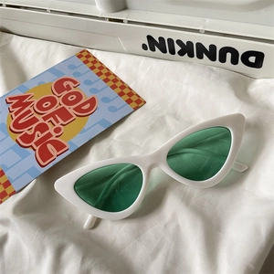 Close-up of retro white cat-eye sunglasses with green lenses on soft white fabric