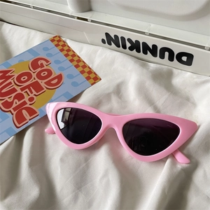 Detailed view of pink cat-eye sunglasses with thick frames on a soft fabric background