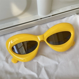 Detailed view of yellow oversized geometric sunglasses with dark brown lenses on white fabric
