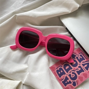 Retro thick pink frame sunglasses with dark lenses displayed on a white fabric background