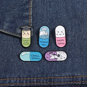 Five unique enamel pharmacy school survivor and vitamin sea pill brooches on denim fabric