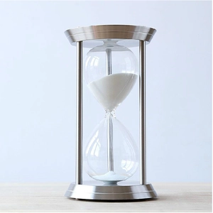 Macro view of silver brushed metal frame and glass hourglass with white sand