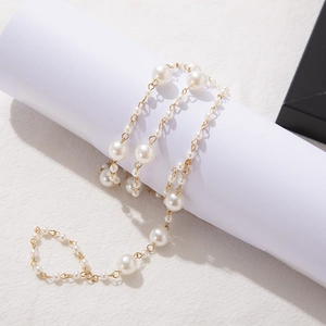 Detail of bohemian gold chain anklet with white pearls draped on a white textured background