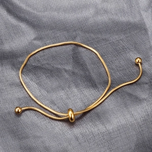 Adjustable gold snake chain bracelet with sliding ball clasp on gray fabric background