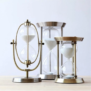 Three metal hourglass timers in brass, silver, and bronze finishes with white sand detail