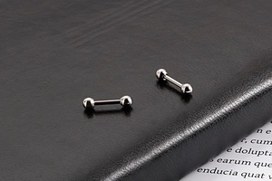 Vue macro de boucles d'oreilles barbell argentées à vis sur surface texturée