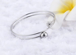 Detail of silver double-layer steel open bangle with sparkling pave ball on soft white plush