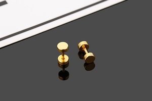 Macro shot of gold dumbbell-style stud earrings with polished finish on a black mirror surface