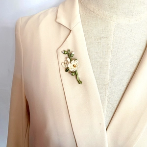Close-up of vintage enamel camellia flower brooch with pearl on a beige blazer lapel