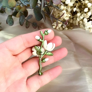 Detailed close-up of a vintage enamel camellia brooch with freshwater pearls and green leaves