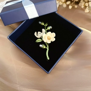 Detail view of vintage enamel flower brooch with freshwater pearl in a blue jewelry box