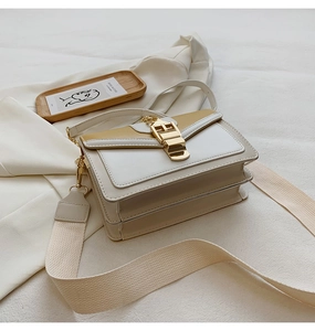 Detail of color-block crossbody bag with wide woven strap and gold buckle on blazer