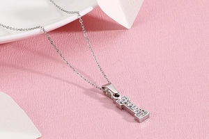 Macro d'un pendentif lettre I en argent avec zircones sur un fond rose texturé