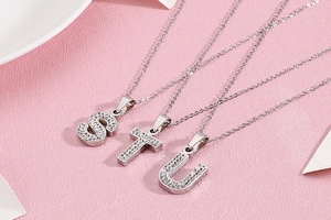 Détail de pendentifs lettres S, T, U en argent avec strass brillants sur fond rose