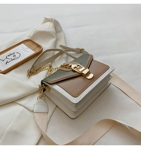 Detail of color-block crossbody bag with gold hardware on white blazer and art decor