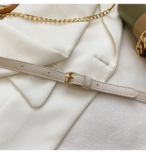 Detail of cream leather shoulder strap with gold buckle and chain on textured fabric