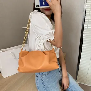 Detail view of orange pleated cloud bag with chunky gold chain strap worn by a model