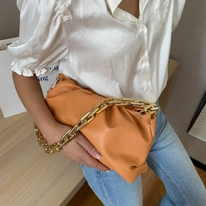 Detail of orange cloud bag featuring a thick gold chain strap held by a model