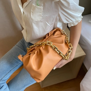 Orange pleated leather cloud bag featuring a chunky gold chain strap worn by a model