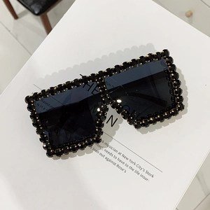 Detail of oversized black sunglasses frame with hand-set rhinestones on white background
