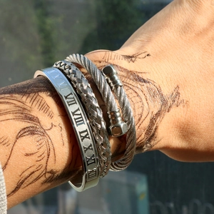 Detailed close-up of silver steel Roman numeral cuff and braided cable bracelet set on wrist