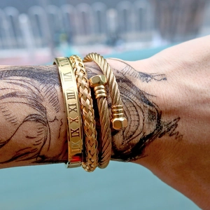 Detailed close-up of a three-piece gold men's bracelet set with Roman numeral engravings