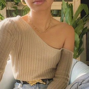 Detail of beige one-shoulder knit top paired with a golden animal buckle belt