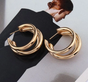 Detail of gold triple-layered intertwined hoop earrings on a fashion magazine background