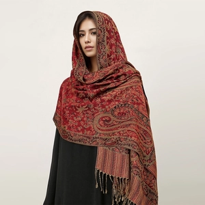 Red paisley cashmere-like scarf with fringe detail worn by model against a white background