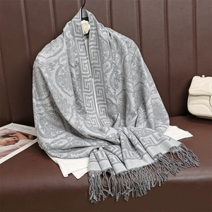 Dettaglio sciarpa jacquard grigia con motivi greci e nappe su un divano in pelle