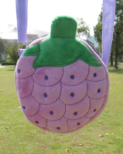 Detail of pink fruit plush crossbody bag with green leaf decoration on green grass