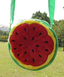 Detail of round watermelon plush crossbody bag with green strap on a grassy background