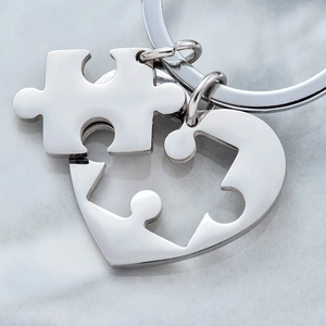 Polished stainless steel heart puzzle keychain set for couples on marble background