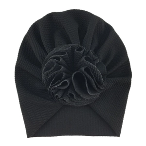 Detailed view of black knitted baby turban with 3D floral decoration on white background