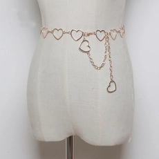 Detail of gold metal heart cutout waist chain with dangling charm on a white mannequin