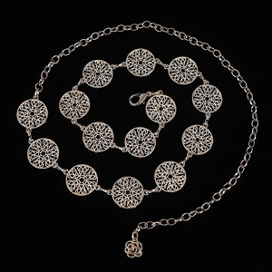 Detail of bohemian gold metal chain belt with hollow circular patterns and rose pendant