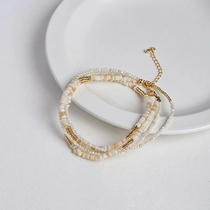 Multilayer beaded necklace with natural shell chips and gold beads on white plate