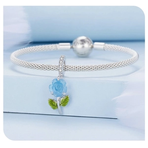 Macro shot of silver charm bracelet with blue rose pendant and green enamel leaf detail